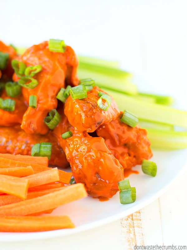 Crispy baked buffalo wings topped with sliced green onions placed on a plate. Served with carrots and celery for a refreshing and robust meal.