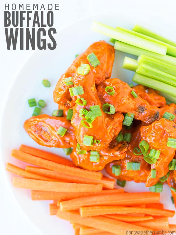 Crispy baked chicken wings topped with buffalo sauce and sliced green onions on a plate with carrots and celery. The text overlay says, "Homemade Buffalo Wings"