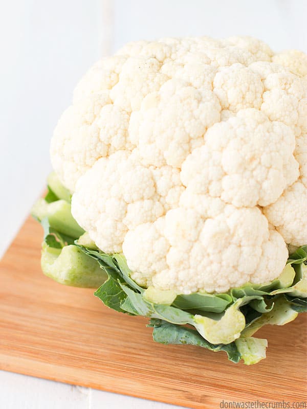 A head of cauliflower on a wooden cutting board.