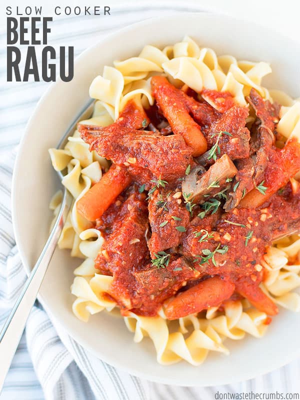 Bowl of pasta topped with beef ragu and baby carrots. Text overlay says, "Slow Cooker Beef Ragu".