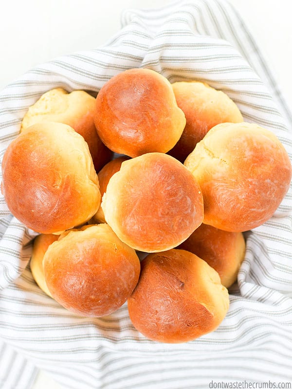 Fluffy cloud dinner rolls, topped with butter, in a pile, on top of a towel. 