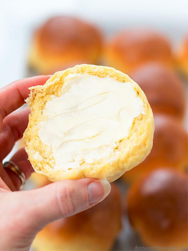 A slice of a fluffy cloud dinner rolls, spread with butter, held by a woman's hand. More cloud rolls are in the background.