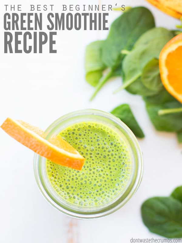 Green Smoothie in a mason jar from the top, with an orange slice on the mason jar. Surrounded by spinach leaves and another orange slice. The text overlay says, "The Best Beginner's Green Smoothie Recipe."