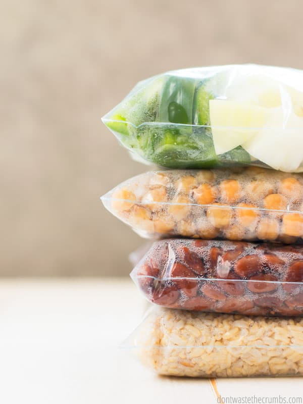 Four Bags of Freezer Cooking prepped food, stacked on top of each other. Food include green peppers and onion, garbanzo beans, pinto beans, and brown rice. 