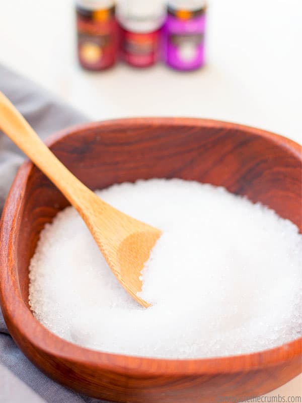 A wooden bowl is filled with sea salt. A wooden spoon dips into the bowl.