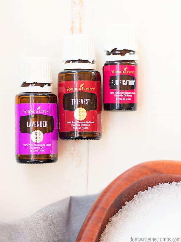 3 essential oil bottles of lavender, thieves, and purification from young living with a bowl of epsom salts.