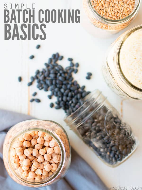 Jars of dried goods on a table. Jars include dried garbanzo beans, orzo, rice and a spilled jar of dried black beans. Text overlay says, "Simple Batch Cooking Basics"