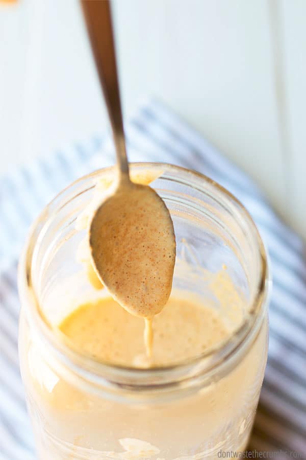 A mason jar of sourdough starter culture being stirred with a spoon. The jar sits on top of a striped kitchen tea towel.