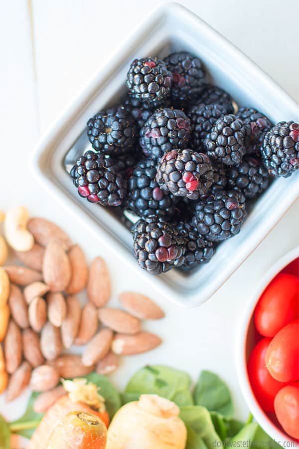 Image of a small bunch of nuts, a bowl of blackberries, bowl of cherry tomatoes, and carrots on top of greens.