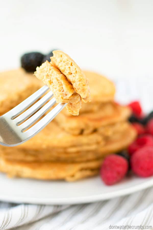 A fork holds a bite of sourdough pancakes, ready to be tasted and enjoyed. There is a stack of pancakes with fresh berries on the plate.