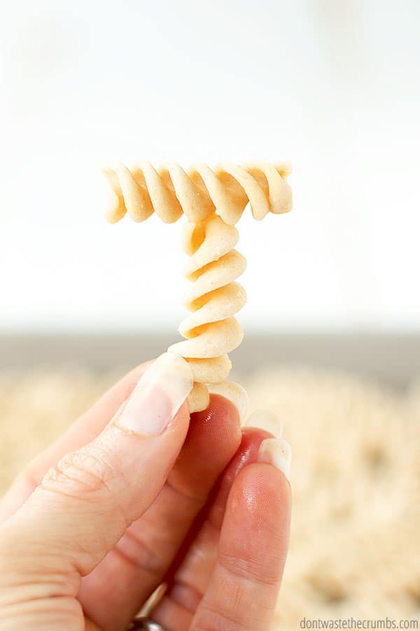 Hand holding two pasta noodles making a letter T