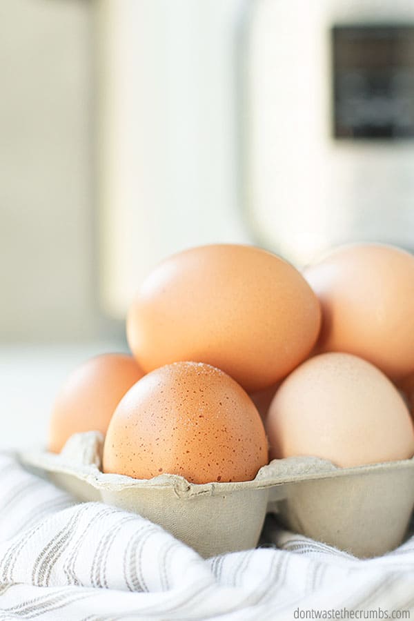 A carton of farm-fresh, speckled brown eggs sits on top of a striped cloth napkin.
