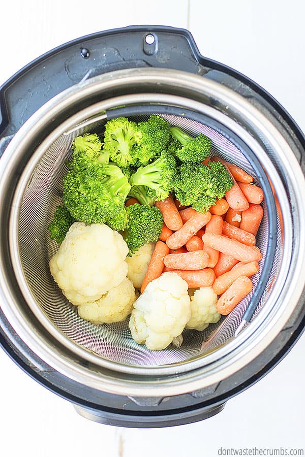 Cooked broccoli florets, baby carrots and chopped cauliflower inside a steaming basket in the Instant Pot.