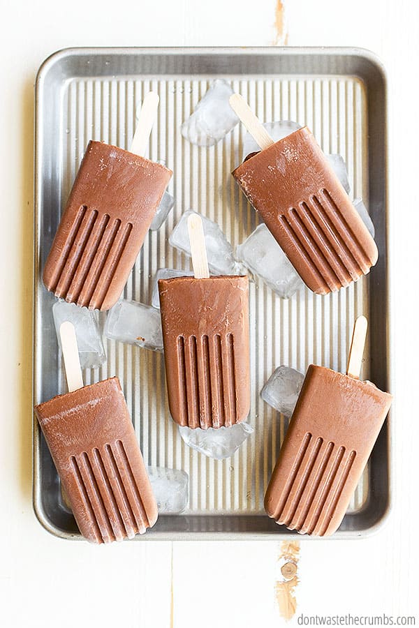 Five fudgesicles lying on ice cubes on a baking sheet