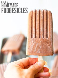 A close-up of a hand holding a homemade fudgesicle, with more fudge pops lying in the background