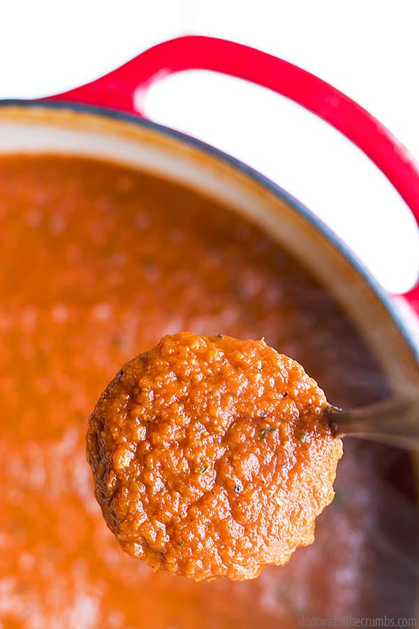 Up close view of a spoonful of homemade tomato sauce. There is a large stockpot with the sauce in it, in the background.