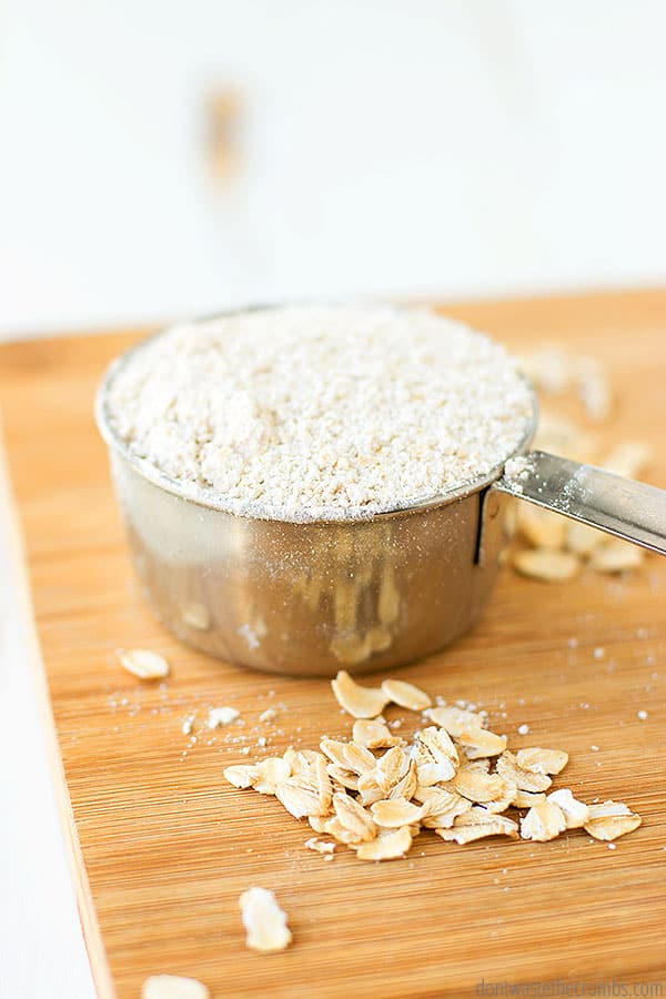 Oat flour in a measuring cup  on a cutting board with some oats next to it