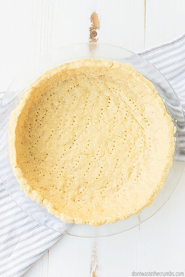 A pie crust in a glass dish, pierced with a fork prior to cooking for proper baking, is cooked to a browned finish.