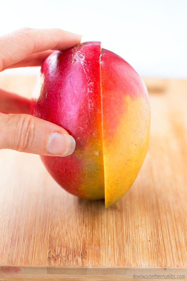 A slice in a mango while being held by a hand on a cutting board.