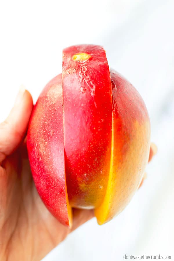 Two slices on a mango with the center raised slightly while being held by a hand.