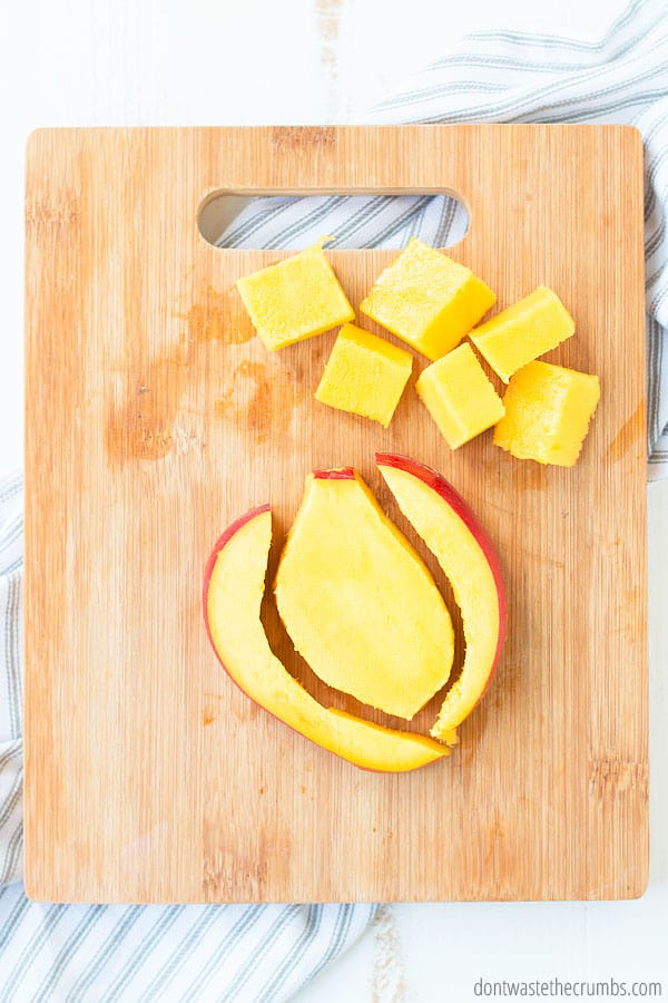 Cubed mango and filet cut mango on a cutting board.