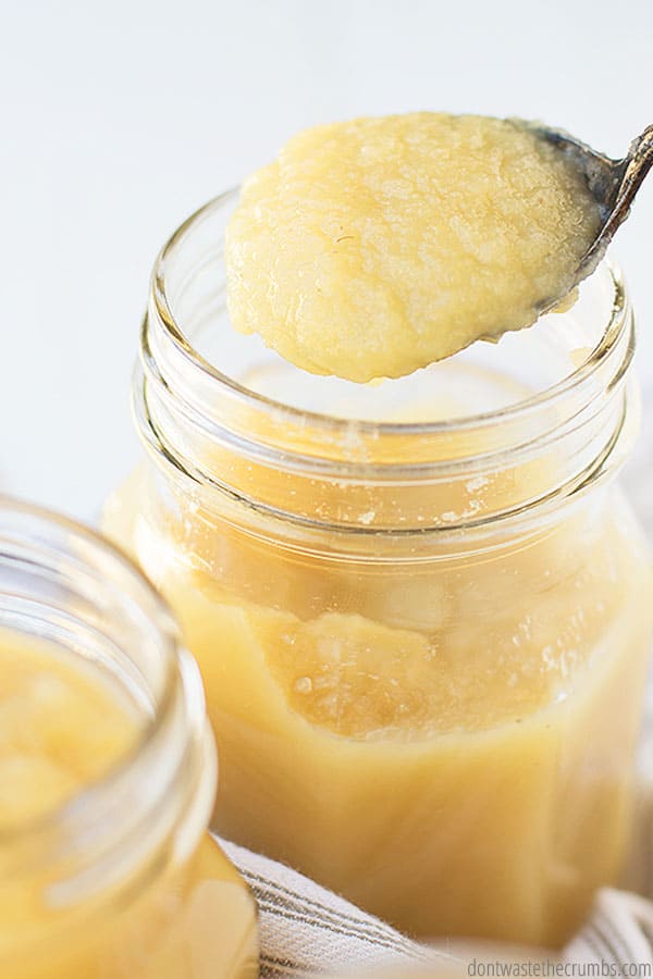Two mason jars are filled with homemade apple sauce. A spoonful of chunky apple sauce hovers above one of the jars.