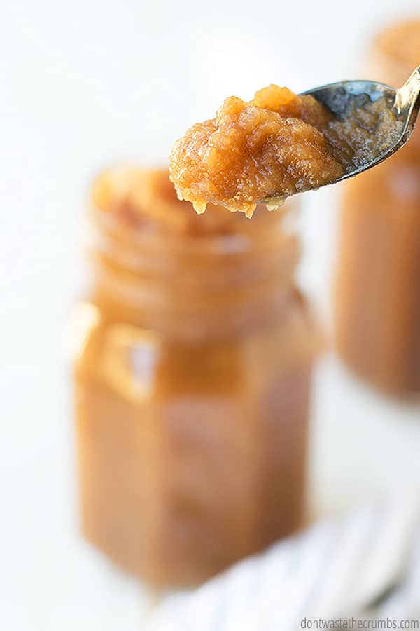 Up close view of spoonful of homemade apple butter. There is a glass jar in the background filled with the same fruit butter.