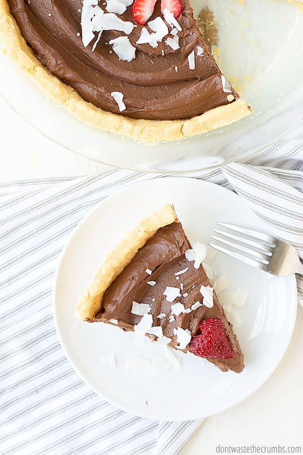 Slice of homemade chocolate pie on a white plate with a fork. The pie is near the slice.