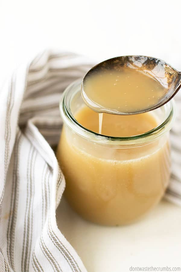 This easy and frugal homemade condensed milk is in a small glass jar as a spoon has been dipped in this tasty mixture!