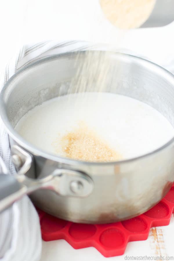 The homemade condensed milk is in the beginning of the process. The milk is in a medium saucepan and sweetener is being added.