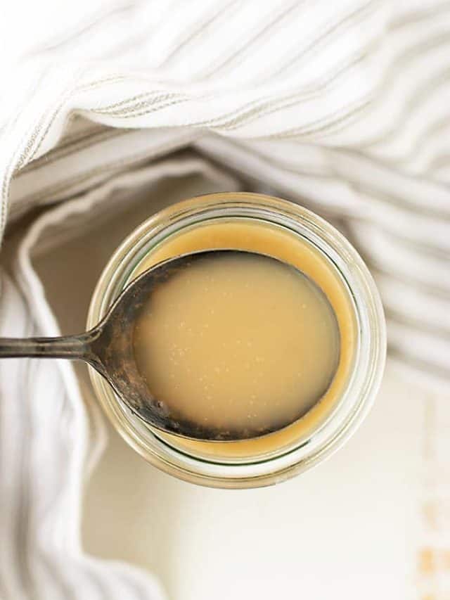 Spoonful of homemade sweetened condensed milk in a glass jar