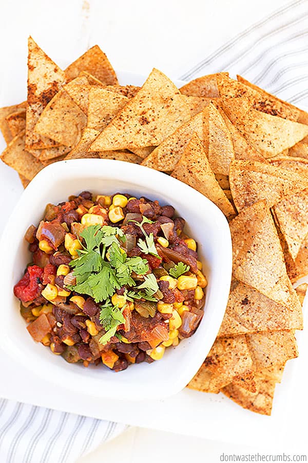 There is a white bowl with black bean and corn salsa and tortilla chips on the side.