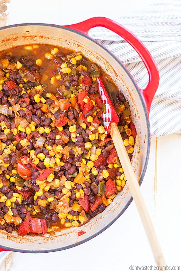 Pot with homemade black bean and corn salsa in it. There is a mixing spoon in the mixture.