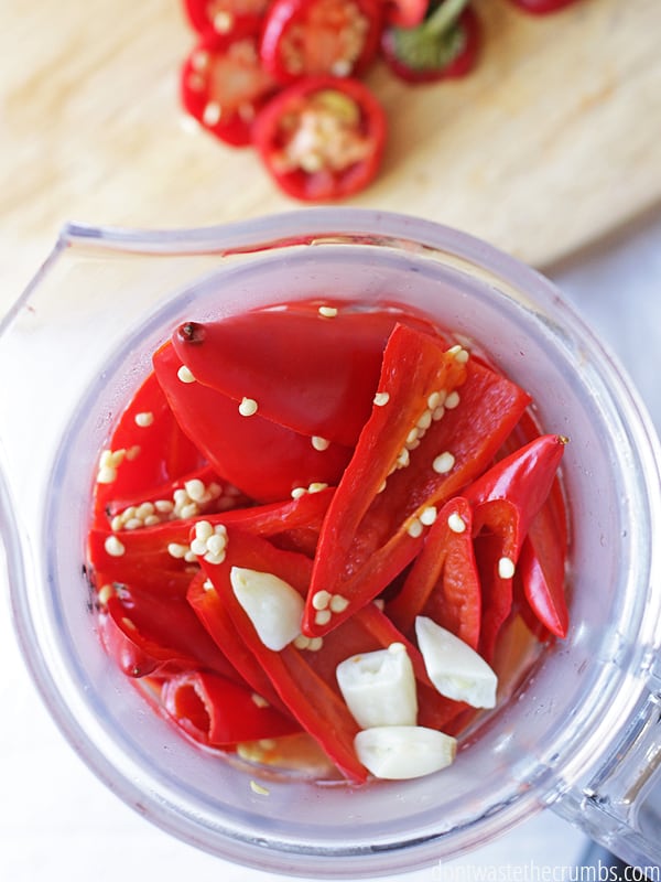 Overview of sliced peppers and seeds and garlic cloves in a blender.