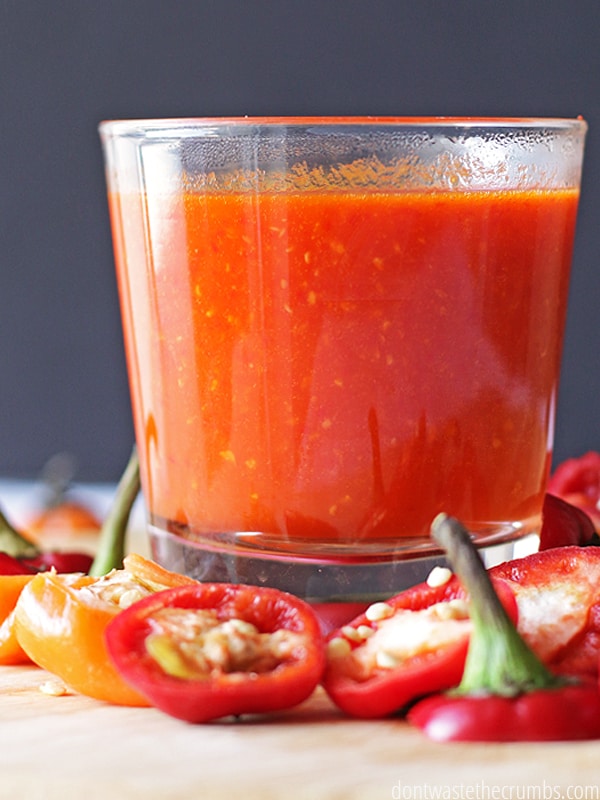 Big glass of homemade hot sauce surrounded by sliced peppers.