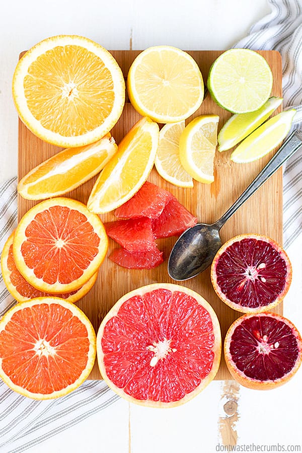Sliced oranges, sliced lemons, sliced limes, sliced strawberries, and sliced grapefruit on a cutting board with a spoon.