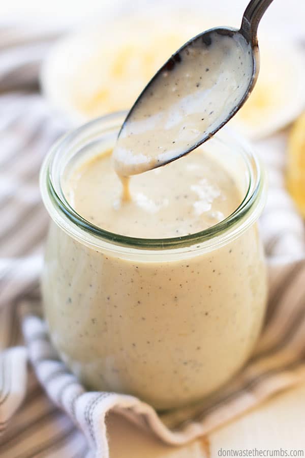 Spoonful of no-mayo Caesar dressing dripping into a glass jar.