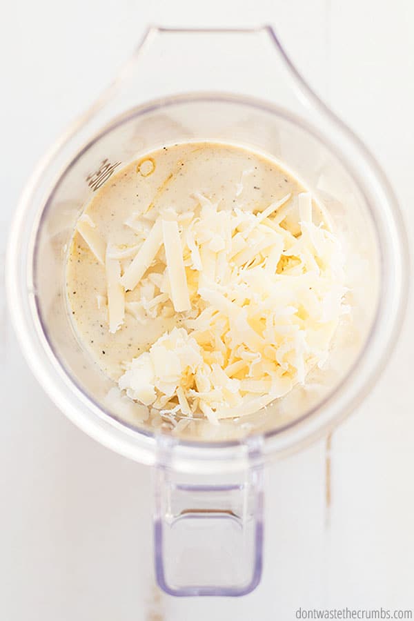 Parmesan cheese sprinkled on top of a liquid mixture that makes no-mayo Caesar dressing in a blender.