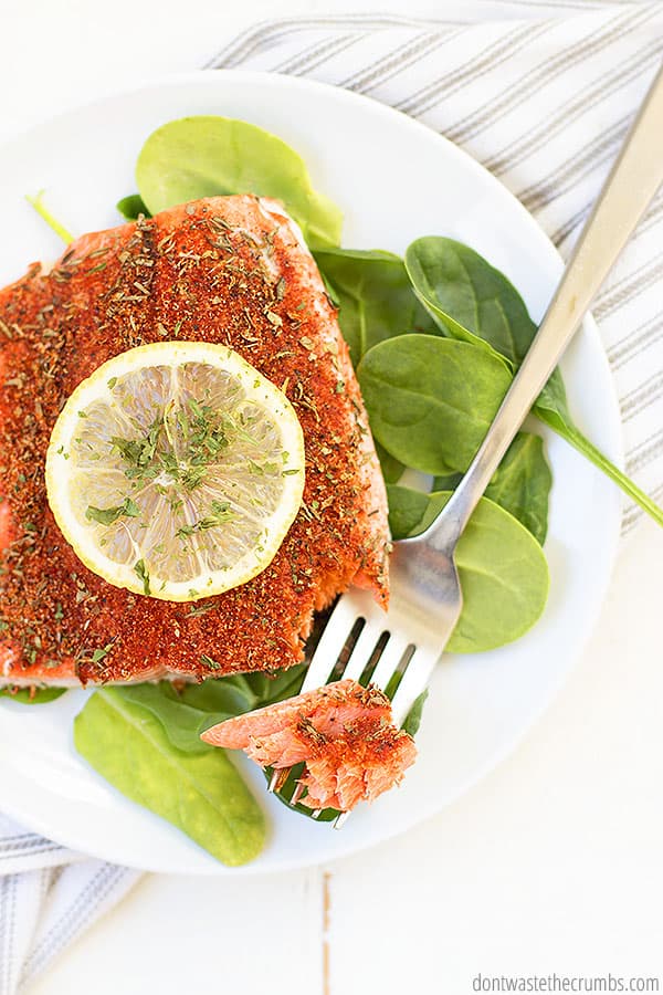 Blackened salmon on a white circle plate and a fork.