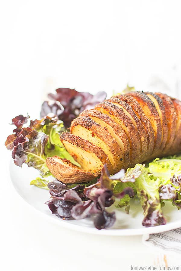 Hasselback potato with lettuce on a white plate.