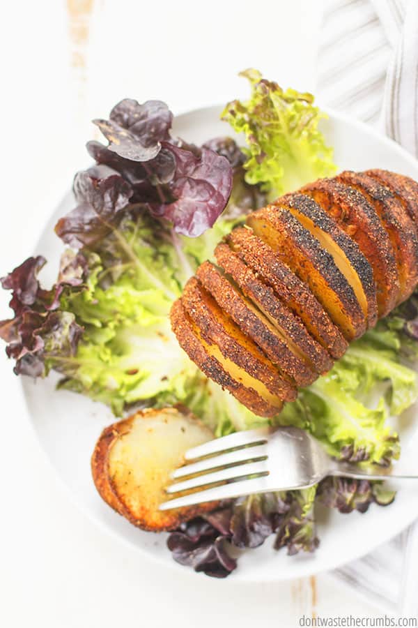 Hasselback potato with lettuce on a white plate. One slice of potato is on a fork.