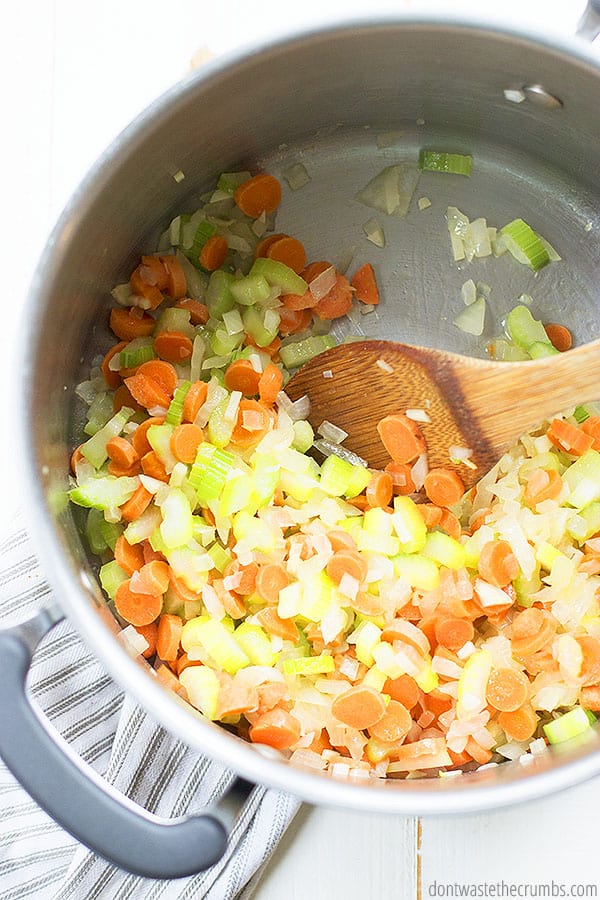 Chopped carrots, celery, onion in a pot being stirred by a wooden spoon.