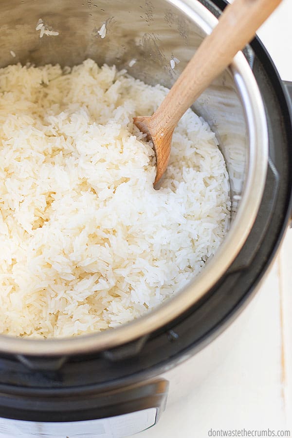 Fluffy and tender white rice cooked inside of an Instant Pot. A wooden spoon is ready to scoop up a serving. 