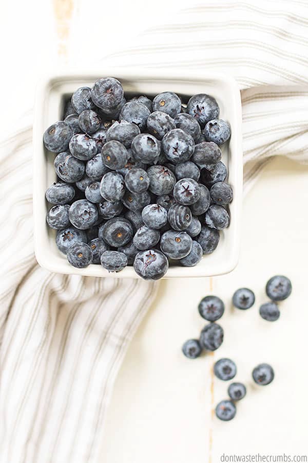 Bowl of blueberries on a tablecloth and a few blueberries on the table