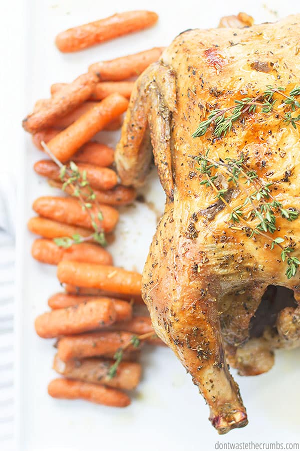 Delicious whole oven roasted chicken with a side of roasted baby carrots on a white plate.