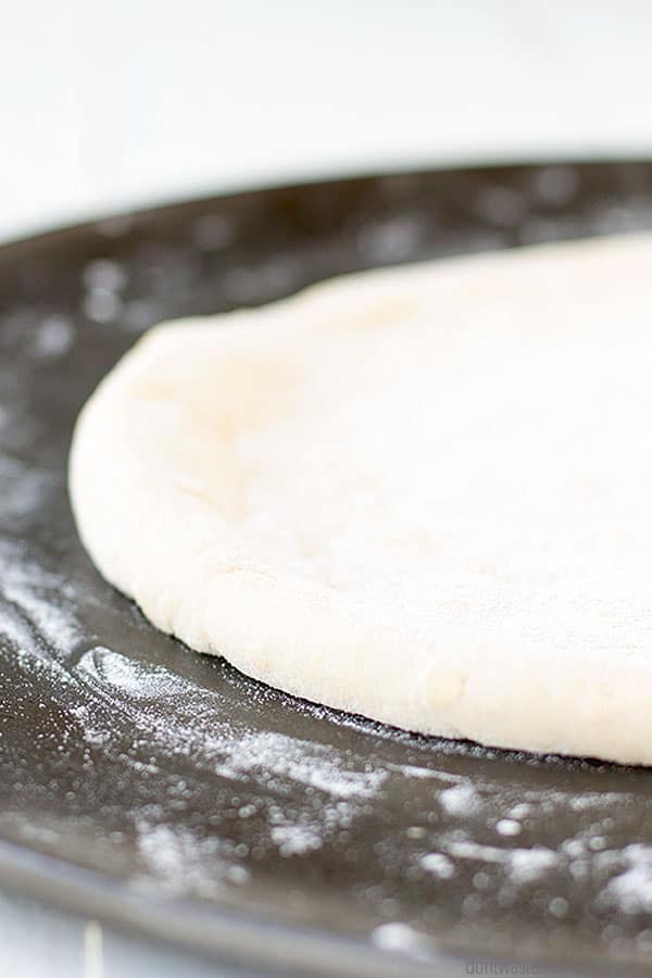 Pizza dough, coated in a fine dusting of flour, is rolled out and ready to bake on a pizza pan.