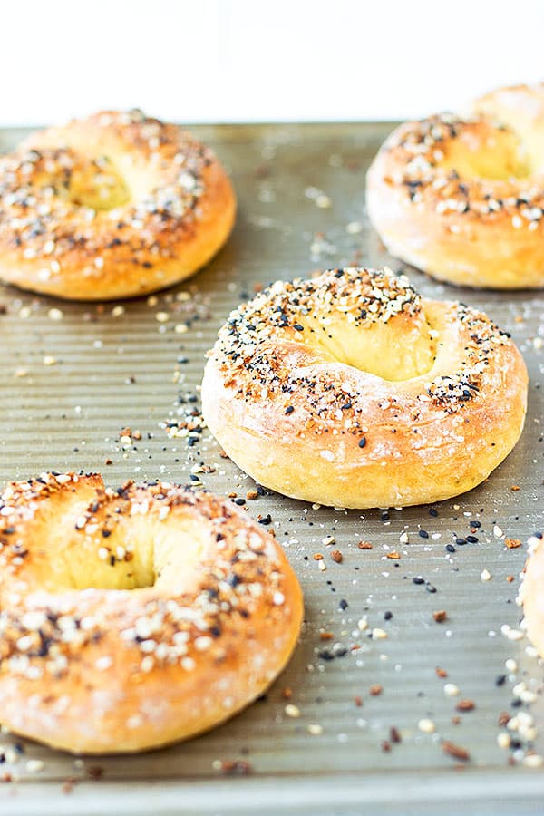 Four homemade bagels with seasoning on top. Laying on a baking sheet.