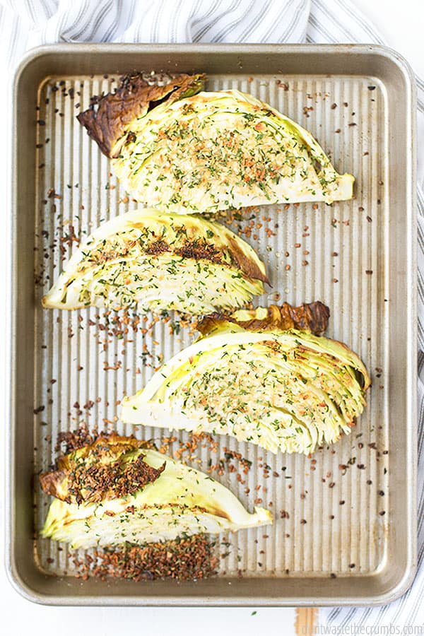 Four roasted cabbage wedges topped with seasoning on a rimmed baking sheet.