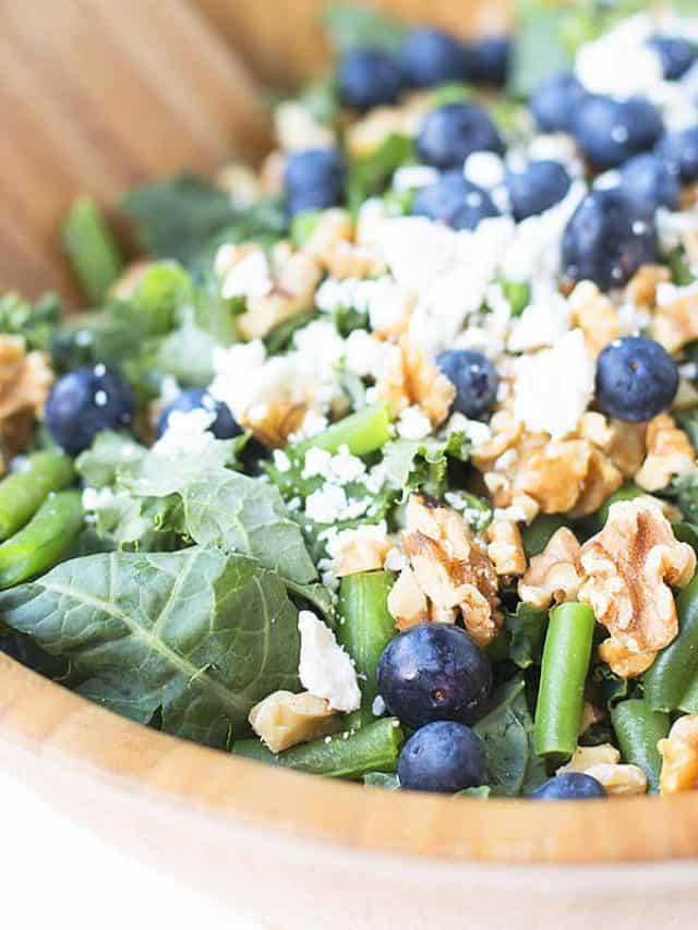 Kale salad with blueberries, walnuts, and feta in a big wooden salad bowl.