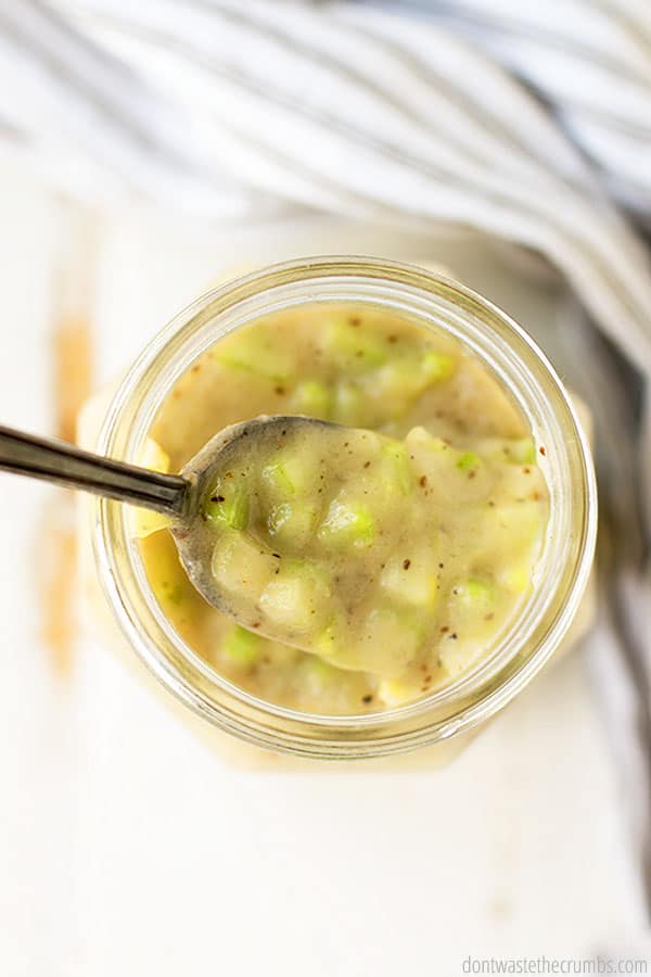 A top view of cream of celery soup in a glass jar with a spoon in it.